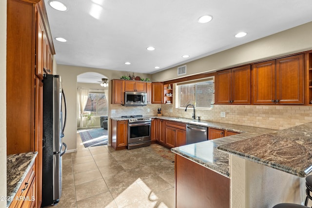 kitchen featuring ceiling fan, kitchen peninsula, sink, appliances with stainless steel finishes, and dark stone counters