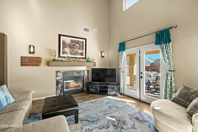 tiled living room with a towering ceiling, french doors, and a stone fireplace