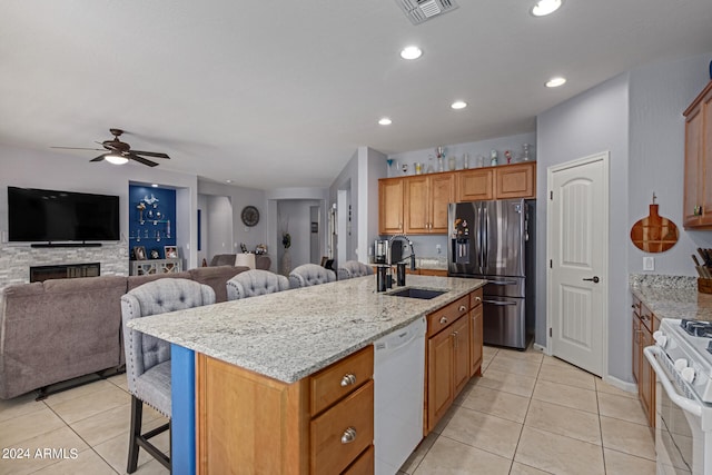 kitchen featuring ceiling fan, a stone fireplace, a kitchen island with sink, and white appliances