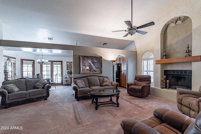 carpeted living room featuring ceiling fan with notable chandelier, a fireplace, high vaulted ceiling, and french doors