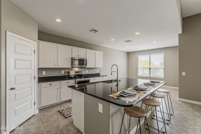 kitchen with dark countertops, a sink, a kitchen island with sink, stainless steel appliances, and visible vents