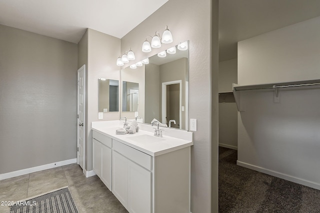 bathroom featuring double vanity, a spacious closet, baseboards, and a sink
