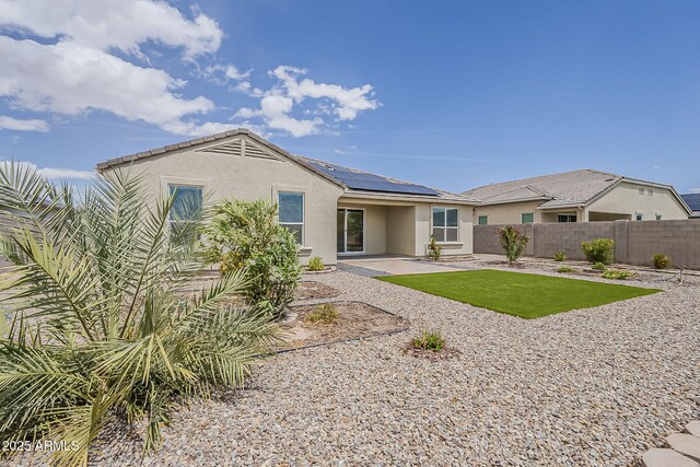 back of house featuring stucco siding, solar panels, fence, and a patio area