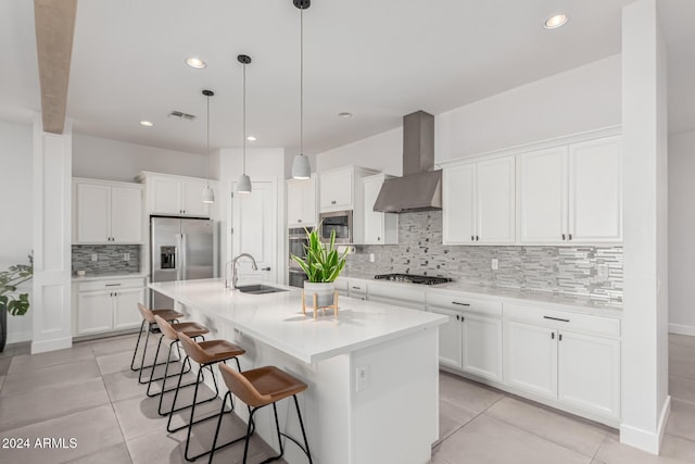 kitchen with appliances with stainless steel finishes, wall chimney exhaust hood, a kitchen island with sink, pendant lighting, and white cabinetry