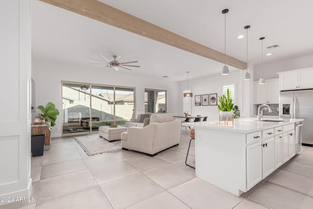 kitchen featuring sink, decorative light fixtures, a center island with sink, beamed ceiling, and white cabinetry