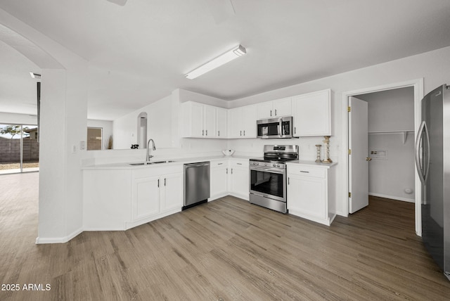 kitchen with appliances with stainless steel finishes, sink, white cabinets, and light hardwood / wood-style floors