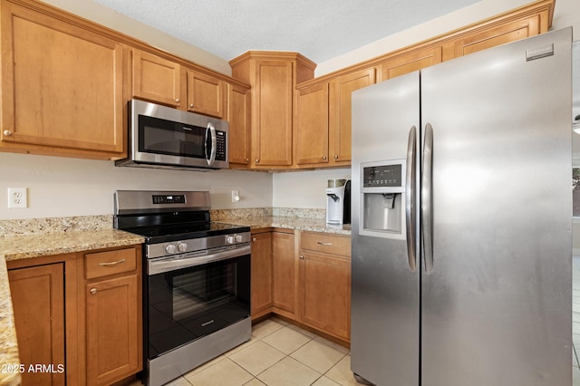 kitchen with light stone counters, a textured ceiling, light tile patterned flooring, and stainless steel appliances