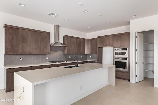 kitchen featuring a sink, wall chimney range hood, double oven, light countertops, and decorative backsplash