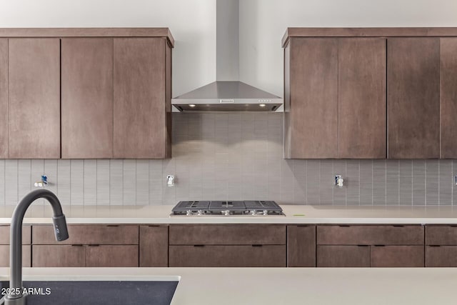kitchen featuring wall chimney range hood, a sink, stainless steel gas cooktop, decorative backsplash, and light countertops