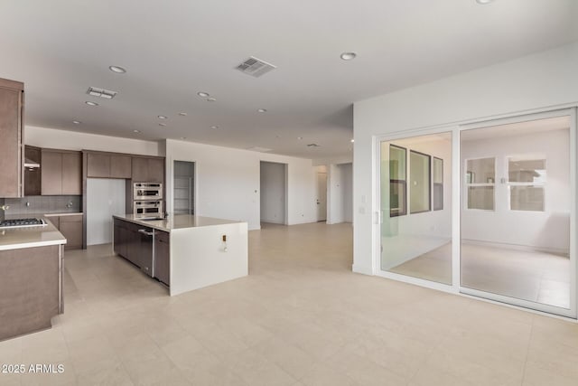 kitchen with open floor plan, light countertops, decorative backsplash, appliances with stainless steel finishes, and a kitchen island with sink