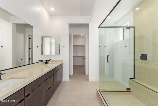 full bathroom with a stall shower, a spacious closet, baseboards, double vanity, and tile patterned flooring