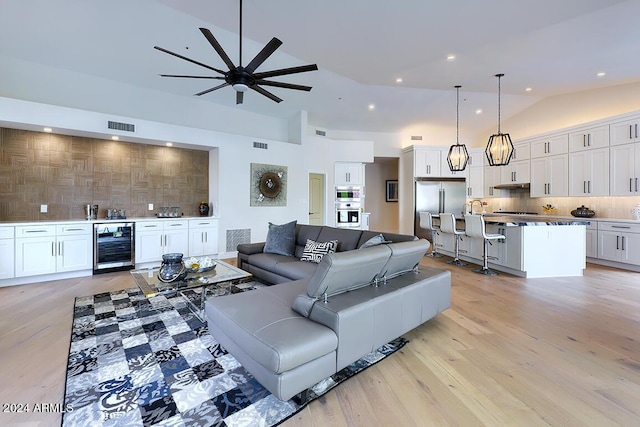 living room with ceiling fan, sink, beverage cooler, lofted ceiling, and light wood-type flooring