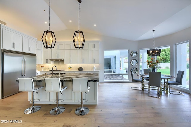 kitchen with white cabinetry, tasteful backsplash, an island with sink, dark stone counters, and stainless steel built in fridge