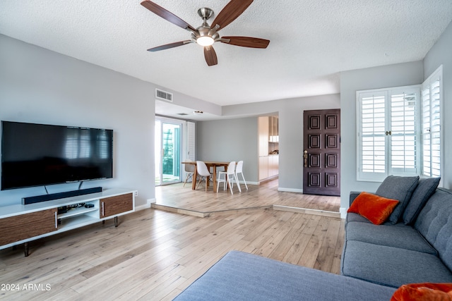 living room with a textured ceiling, a healthy amount of sunlight, light wood-type flooring, and ceiling fan