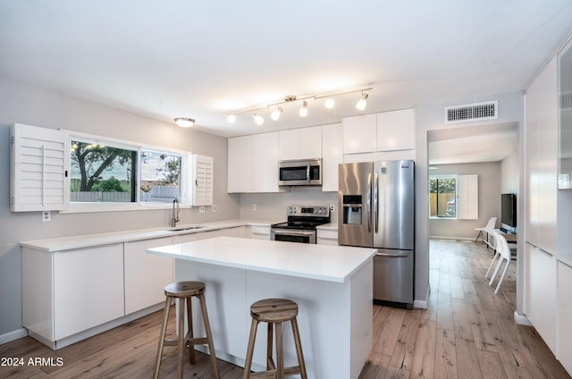 kitchen with white cabinets, appliances with stainless steel finishes, sink, light hardwood / wood-style floors, and a center island