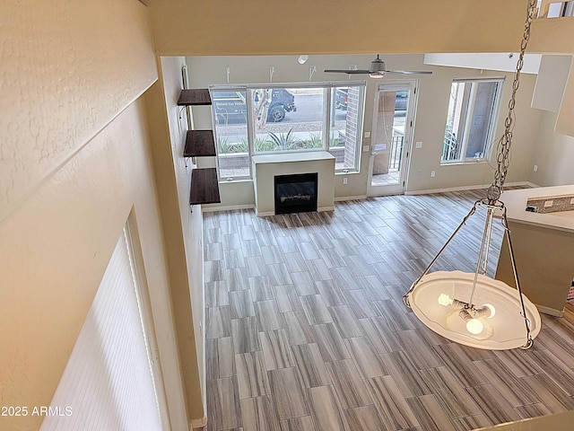 unfurnished living room featuring ceiling fan, baseboards, a glass covered fireplace, and wood tiled floor