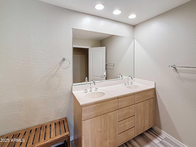 bathroom with wood finished floors, double vanity, a sink, and a textured wall
