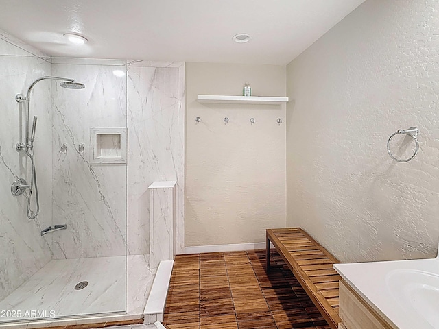 bathroom with baseboards, a marble finish shower, a textured wall, and vanity