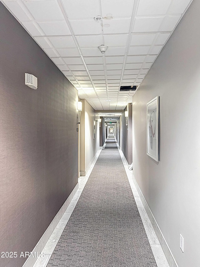 corridor featuring a paneled ceiling and baseboards