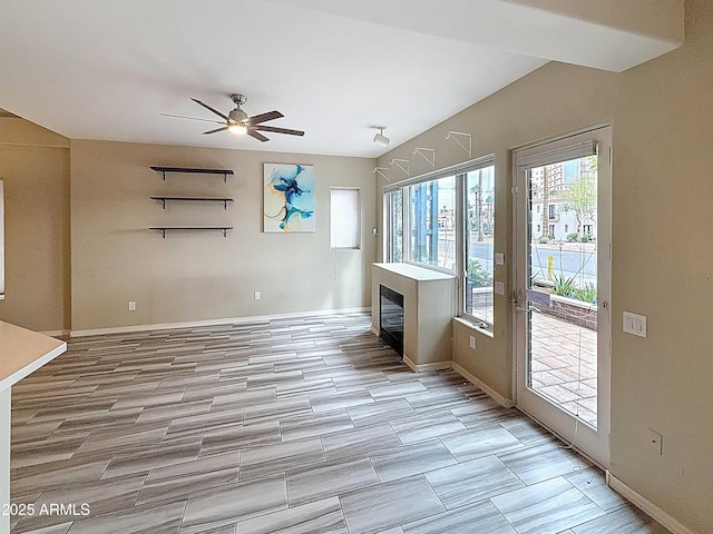 unfurnished living room featuring baseboards, a ceiling fan, and a glass covered fireplace