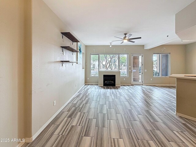 unfurnished living room with baseboards, ceiling fan, a fireplace, and wood finish floors