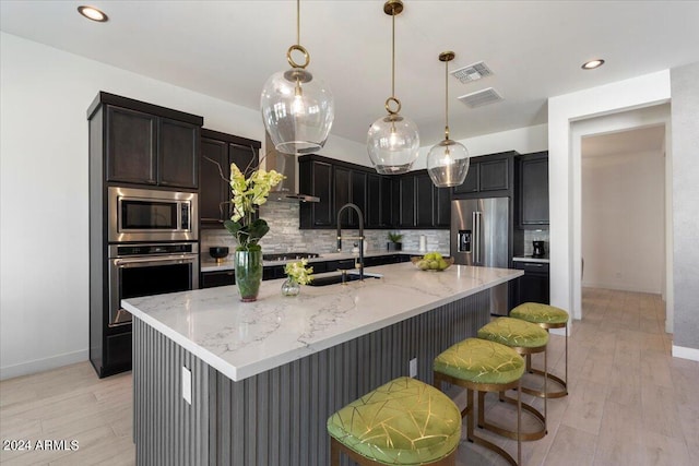 kitchen featuring light hardwood / wood-style floors, a kitchen island with sink, stainless steel appliances, and tasteful backsplash