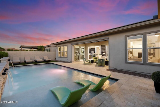 pool at dusk featuring a patio area and pool water feature