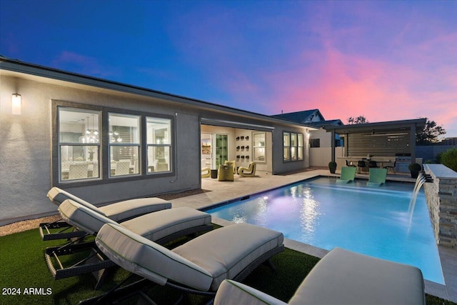 pool at dusk featuring an outdoor kitchen, pool water feature, and a patio area