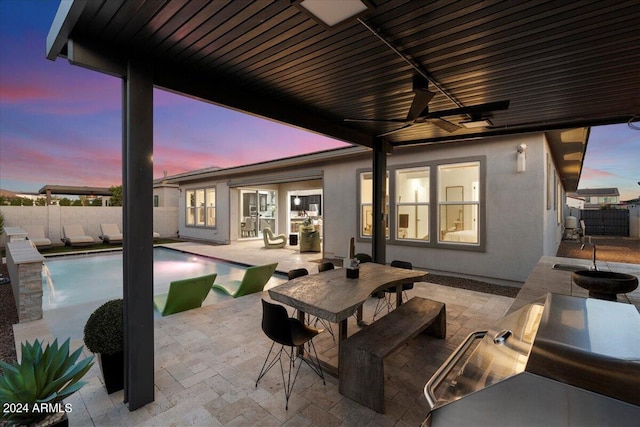 patio terrace at dusk featuring a fenced in pool, pool water feature, and ceiling fan