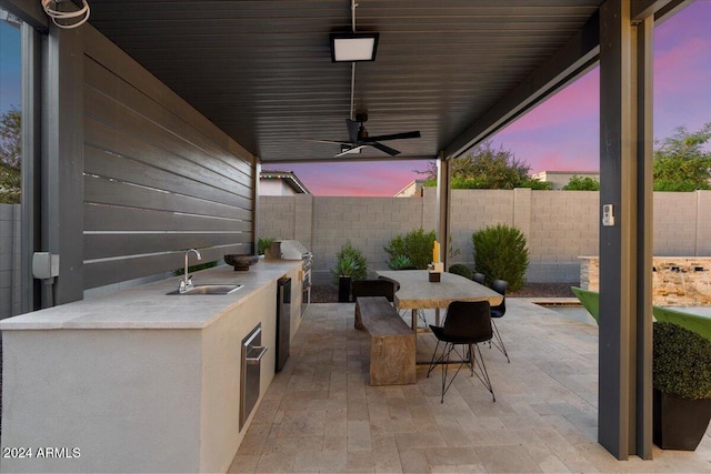 patio terrace at dusk with ceiling fan, sink, and an outdoor kitchen