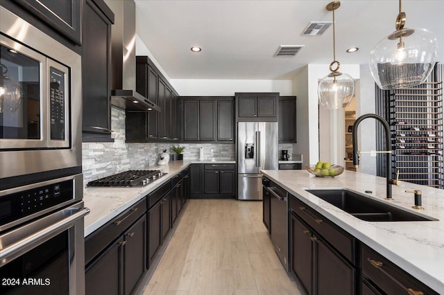 kitchen featuring wall chimney range hood, backsplash, sink, appliances with stainless steel finishes, and light hardwood / wood-style floors