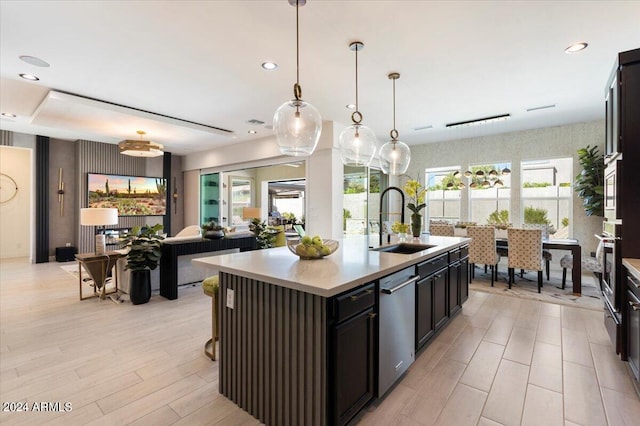 kitchen with appliances with stainless steel finishes, sink, an island with sink, light hardwood / wood-style floors, and decorative light fixtures