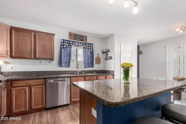 kitchen featuring light wood-style flooring, dishwasher, a kitchen bar, dark stone countertops, and a sink