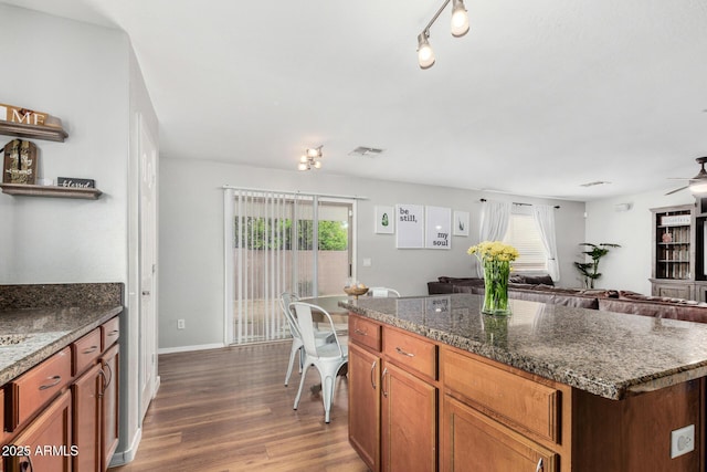 kitchen featuring wood finished floors, open floor plan, baseboards, visible vents, and dark stone counters