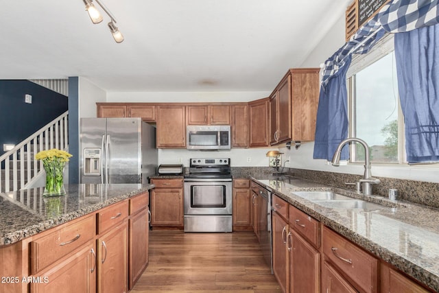 kitchen with dark wood-style flooring, dark stone counters, a sink, appliances with stainless steel finishes, and brown cabinetry