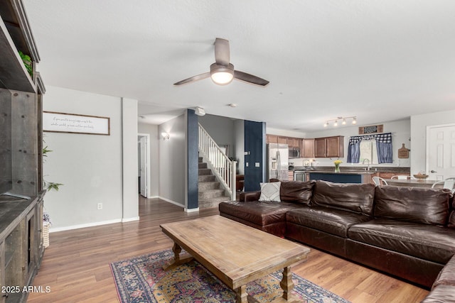 living room featuring a ceiling fan, baseboards, stairway, and wood finished floors