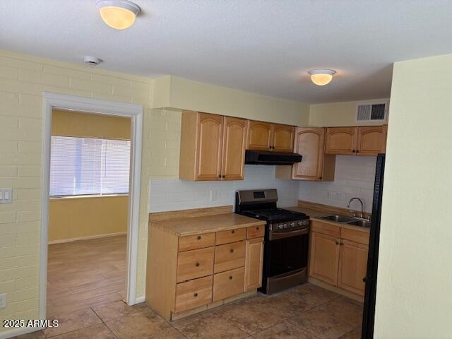 kitchen with gas range, a sink, under cabinet range hood, light countertops, and tasteful backsplash
