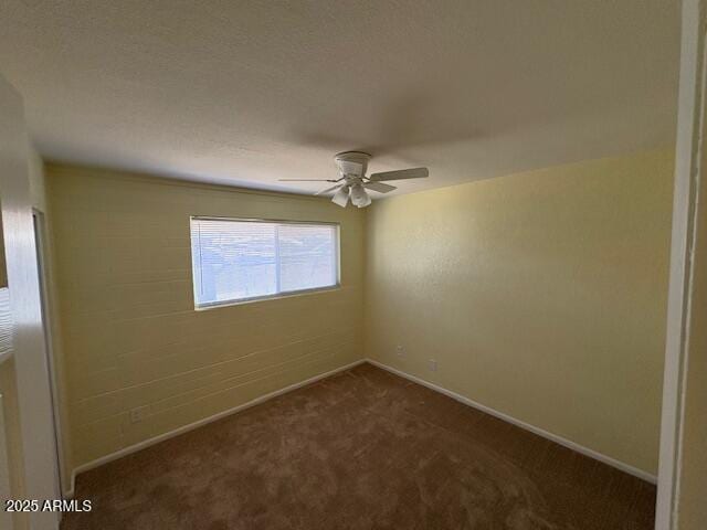 spare room with dark colored carpet, a ceiling fan, and baseboards
