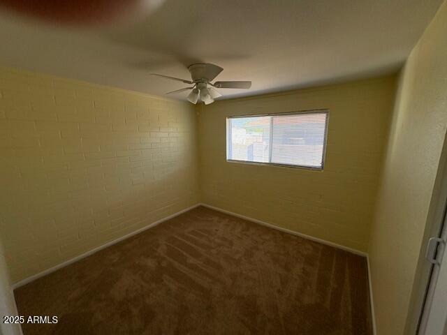 empty room with dark colored carpet, a ceiling fan, and baseboards