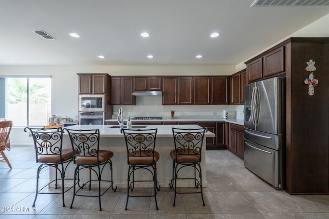 kitchen with a center island with sink, appliances with stainless steel finishes, a kitchen bar, and dark brown cabinets