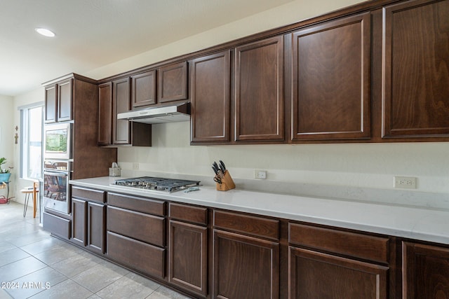 kitchen featuring dark brown cabinets, light tile patterned floors, and stainless steel appliances