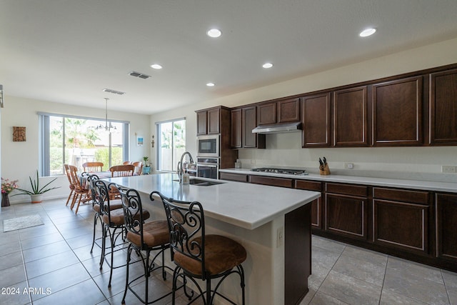 kitchen with a kitchen island with sink, a breakfast bar, decorative light fixtures, sink, and appliances with stainless steel finishes