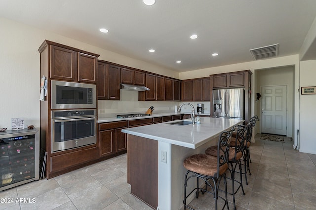 kitchen featuring wine cooler, sink, a center island with sink, appliances with stainless steel finishes, and a kitchen bar