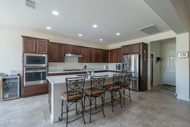 kitchen with wine cooler, an island with sink, sink, appliances with stainless steel finishes, and a kitchen breakfast bar