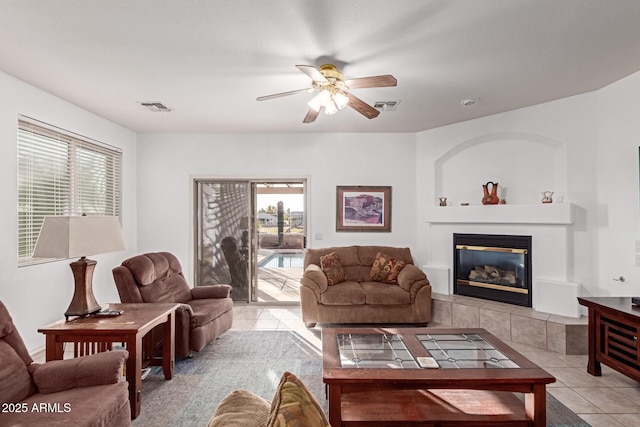 living room with light tile patterned flooring, a tile fireplace, visible vents, and a ceiling fan