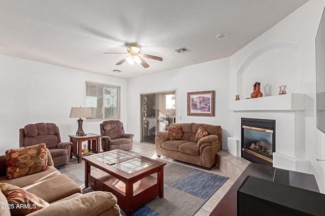 living room featuring ceiling fan, light tile patterned flooring, a glass covered fireplace, and visible vents