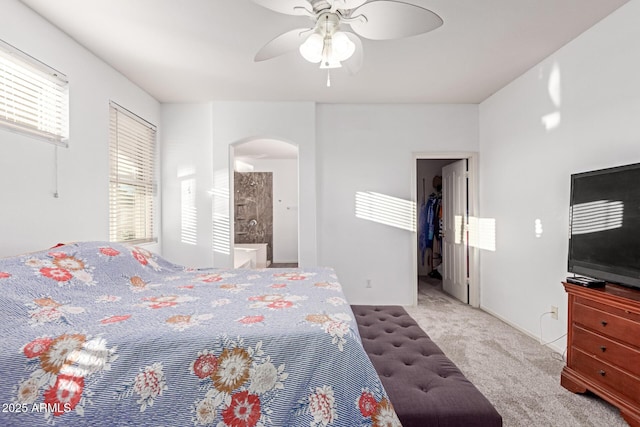 bedroom featuring arched walkways, a walk in closet, carpet, a ceiling fan, and ensuite bath