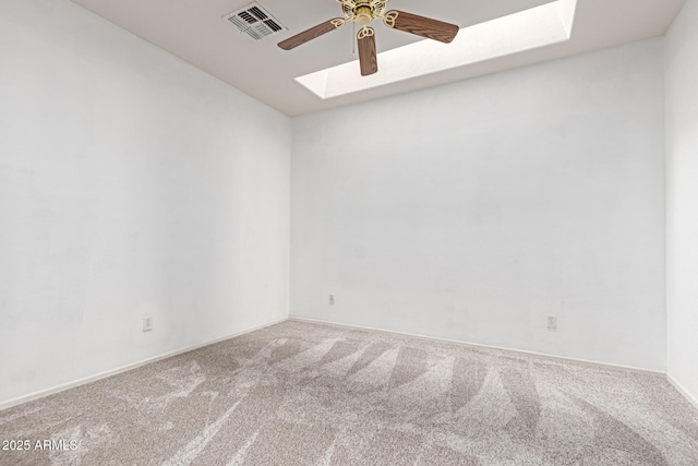 carpeted spare room with a skylight, visible vents, ceiling fan, and baseboards