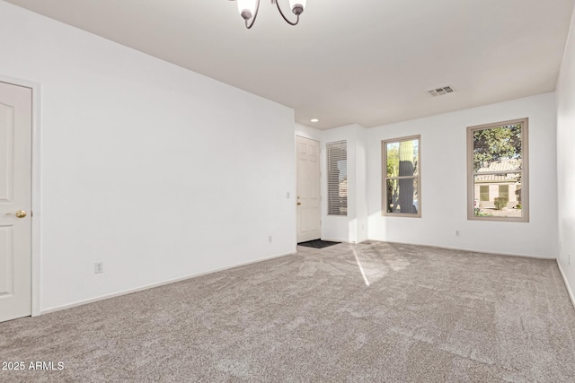 carpeted empty room featuring visible vents, baseboards, and an inviting chandelier