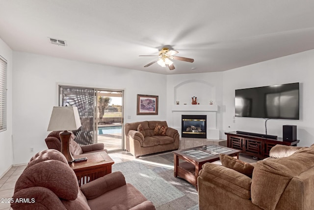 living area with ceiling fan, light tile patterned flooring, a tile fireplace, and visible vents